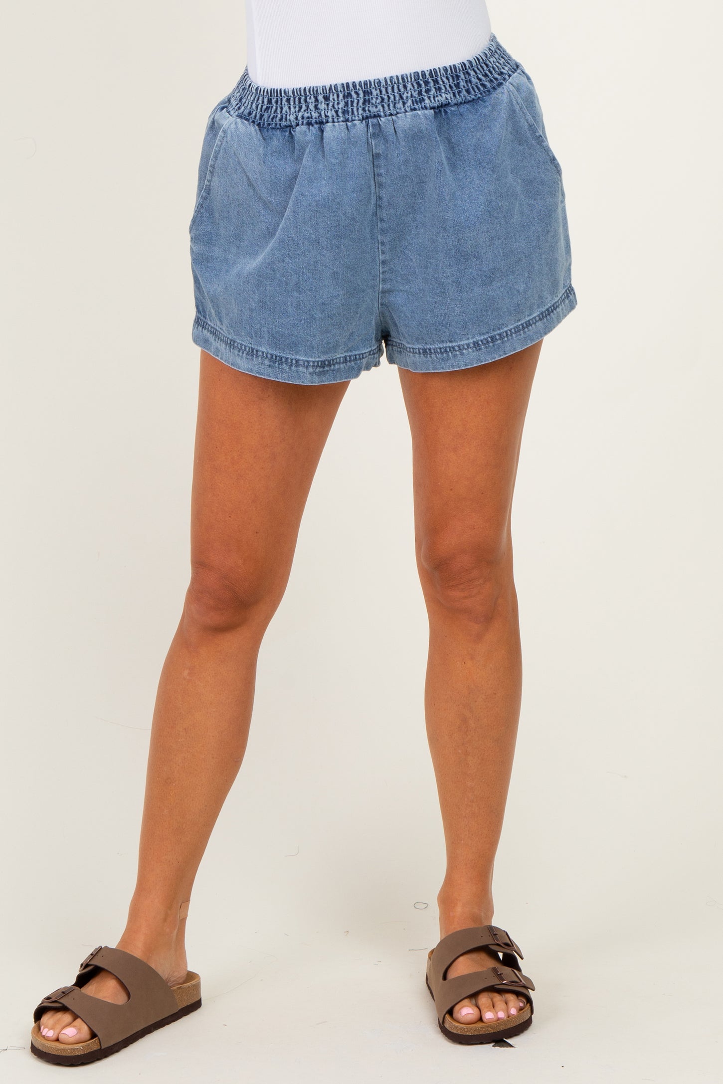 woman wearing light blue denim shorts with an elastic waistband and side pockets, styled casually with brown sandals