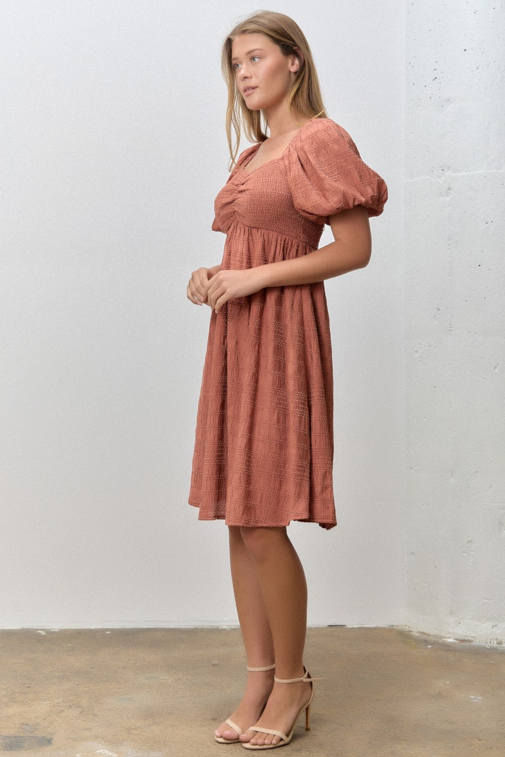 woman wearing a rust-colored knee-length dress with puff sleeves and a fitted bodice