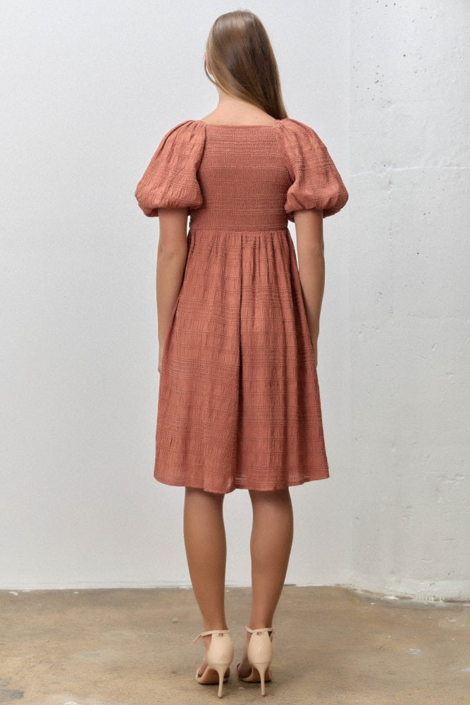 woman wearing a rust-colored puff sleeve dress with a smocked bodice and a flared skirt, viewed from the back