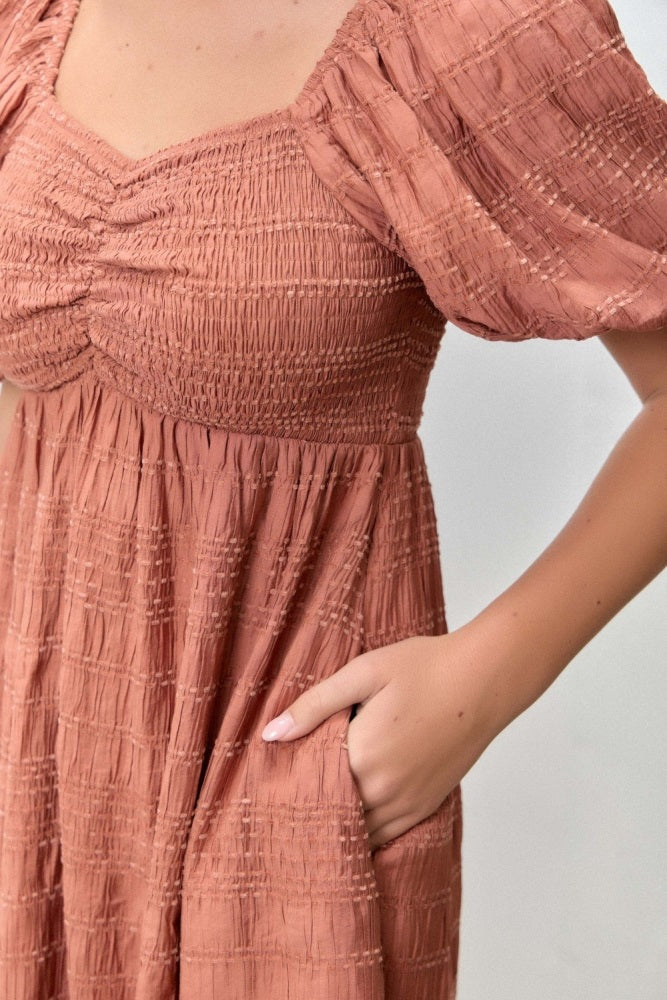 woman wearing a terracotta smocked midi dress with puff sleeves and side pockets