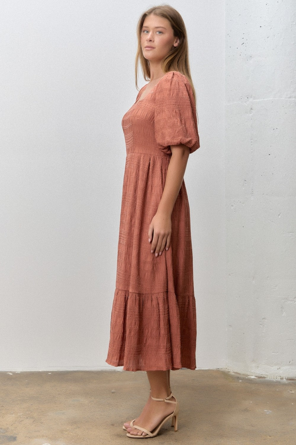 woman wearing a rust-colored midi dress with puff sleeves and tiered skirt, standing against a neutral backdrop