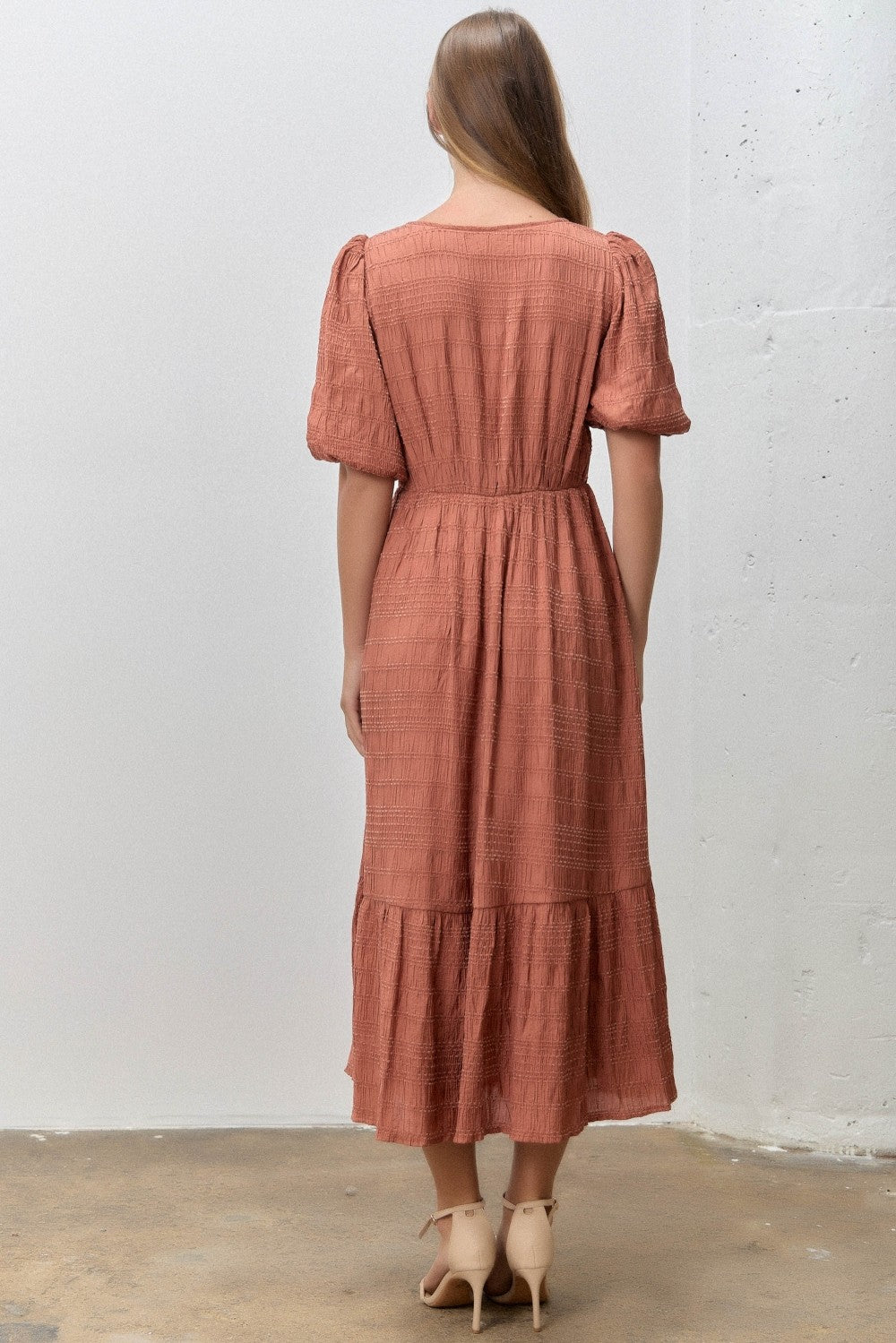 woman wearing a rust colored mid-length dress with puff sleeves and a tiered bottom, seen from the back