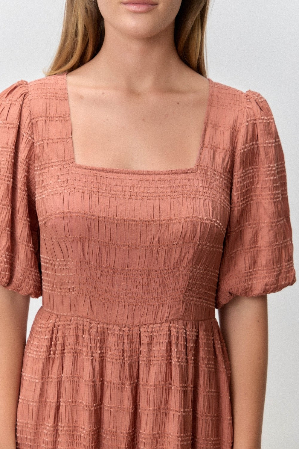woman wearing a rust-colored square neck dress with puff sleeves and textured detailing
