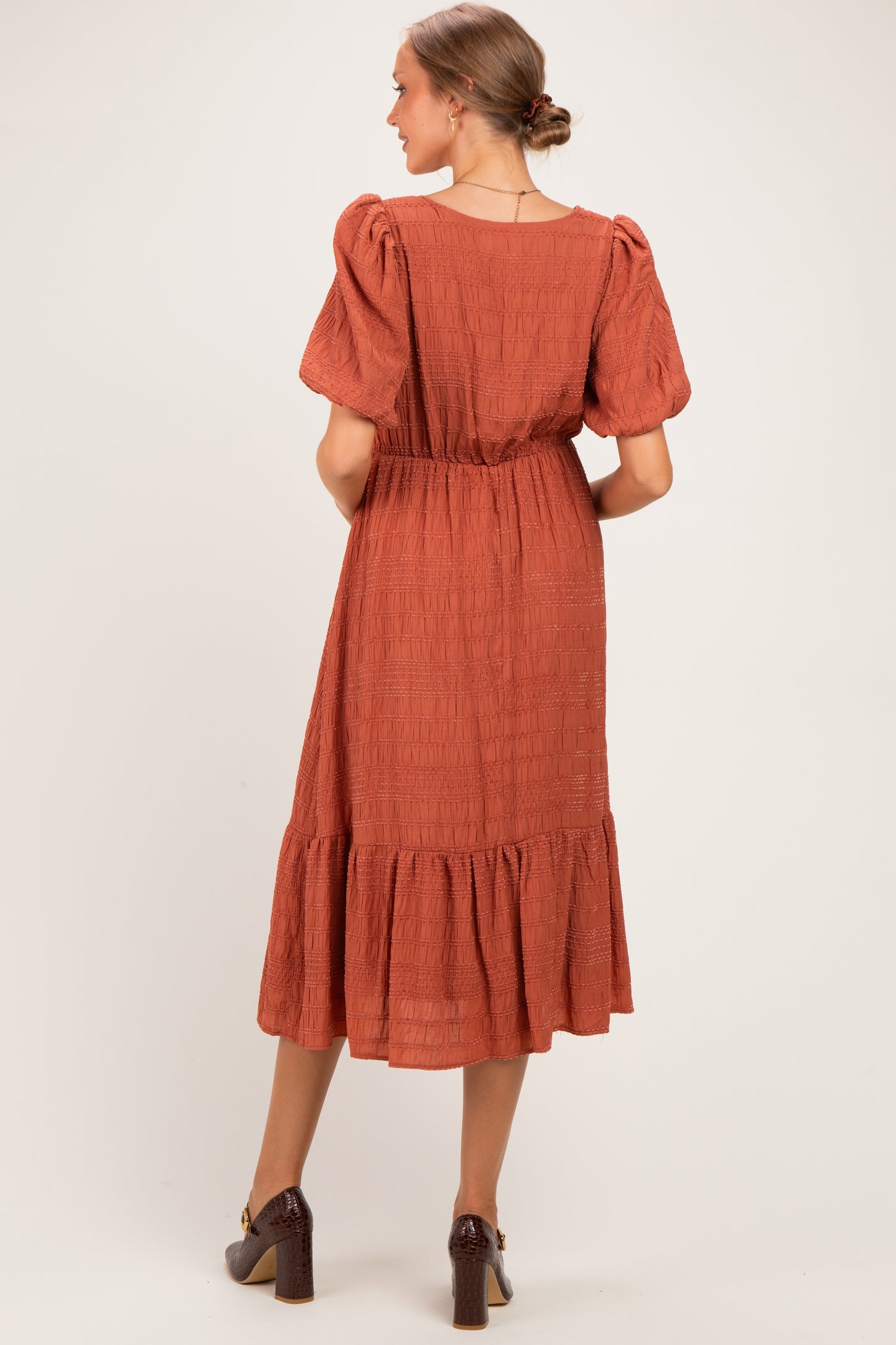 woman wearing a rust-colored maternity dress with puff sleeves and a tiered skirt, seen from the back