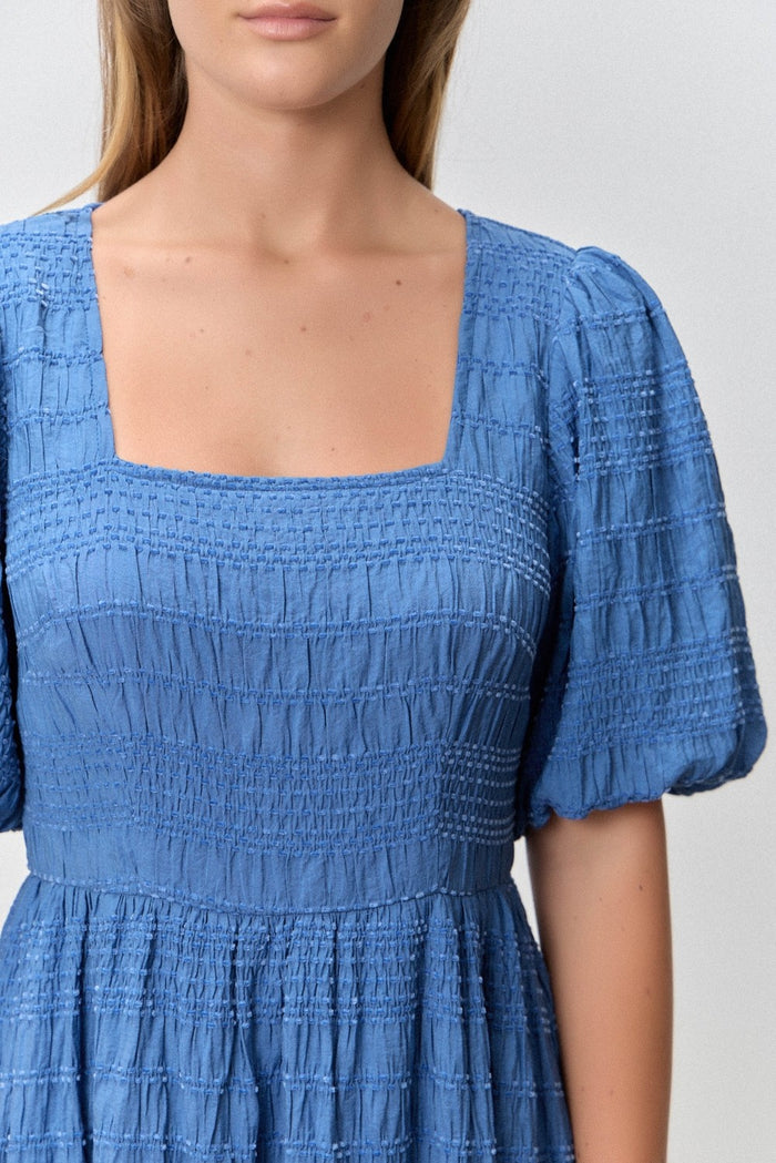 woman wearing a blue smocked top with short puff sleeves and a square neckline