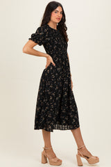 woman wearing a black floral midi dress with puff sleeves and a cinched waist, paired with nude platform heels