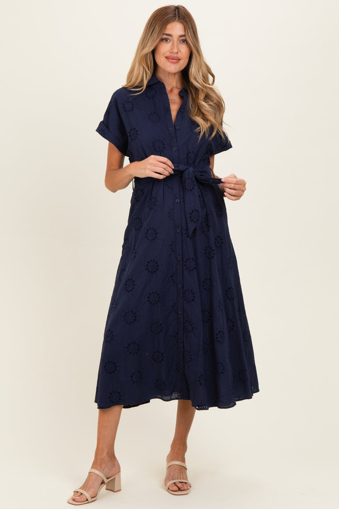 woman wearing a navy blue short sleeve maternity dress with an embroidered floral pattern and a tied waist