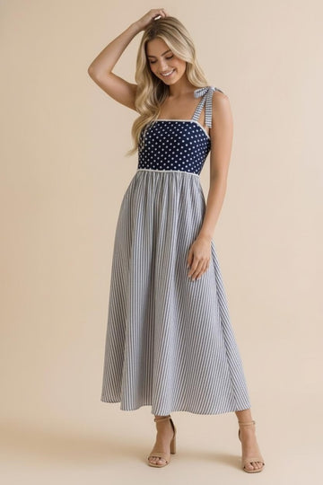 woman wearing a navy and white polka dot and striped maxi dress with tie shoulder straps and a flared skirt