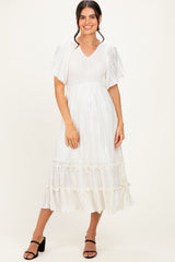 woman wearing a white pleated midi dress with short puff sleeves and a tiered hem, styled with black heeled sandals