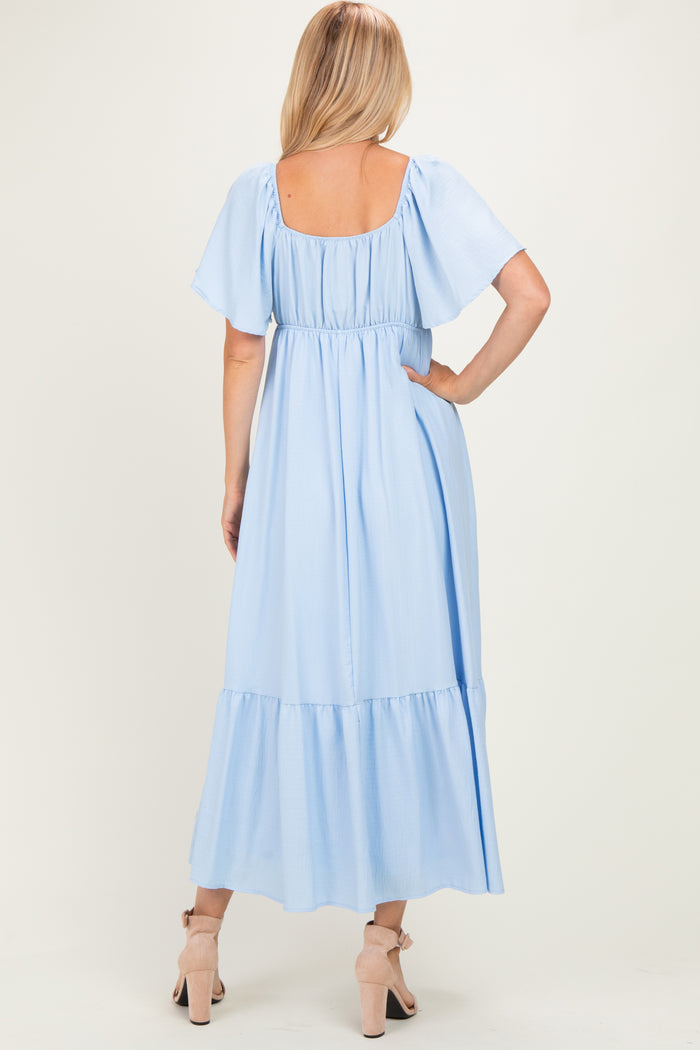 woman wearing a light blue maxi dress with short flutter sleeves and a tiered skirt, viewed from the back