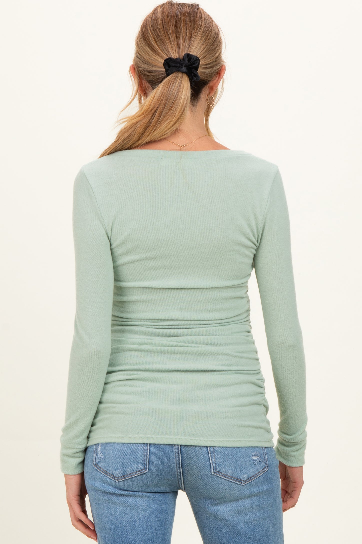 woman wearing a light green long sleeve maternity top with a fitted silhouette and gathered detailing at the sides