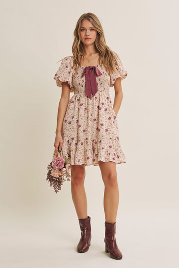 woman wearing a floral print dress with puff sleeves and a bow detail, holding a bouquet of flowers
