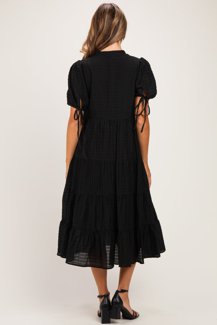 woman wearing a black tiered maternity dress with puff sleeves and tie details at the arms