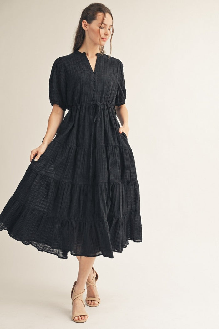 woman wearing a black tiered maxi dress with a button-down front and puff sleeves, standing gracefully