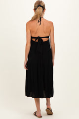 woman wearing a black halter neck maternity dress with a tie-back detail and flared skirt, showing a baby bump