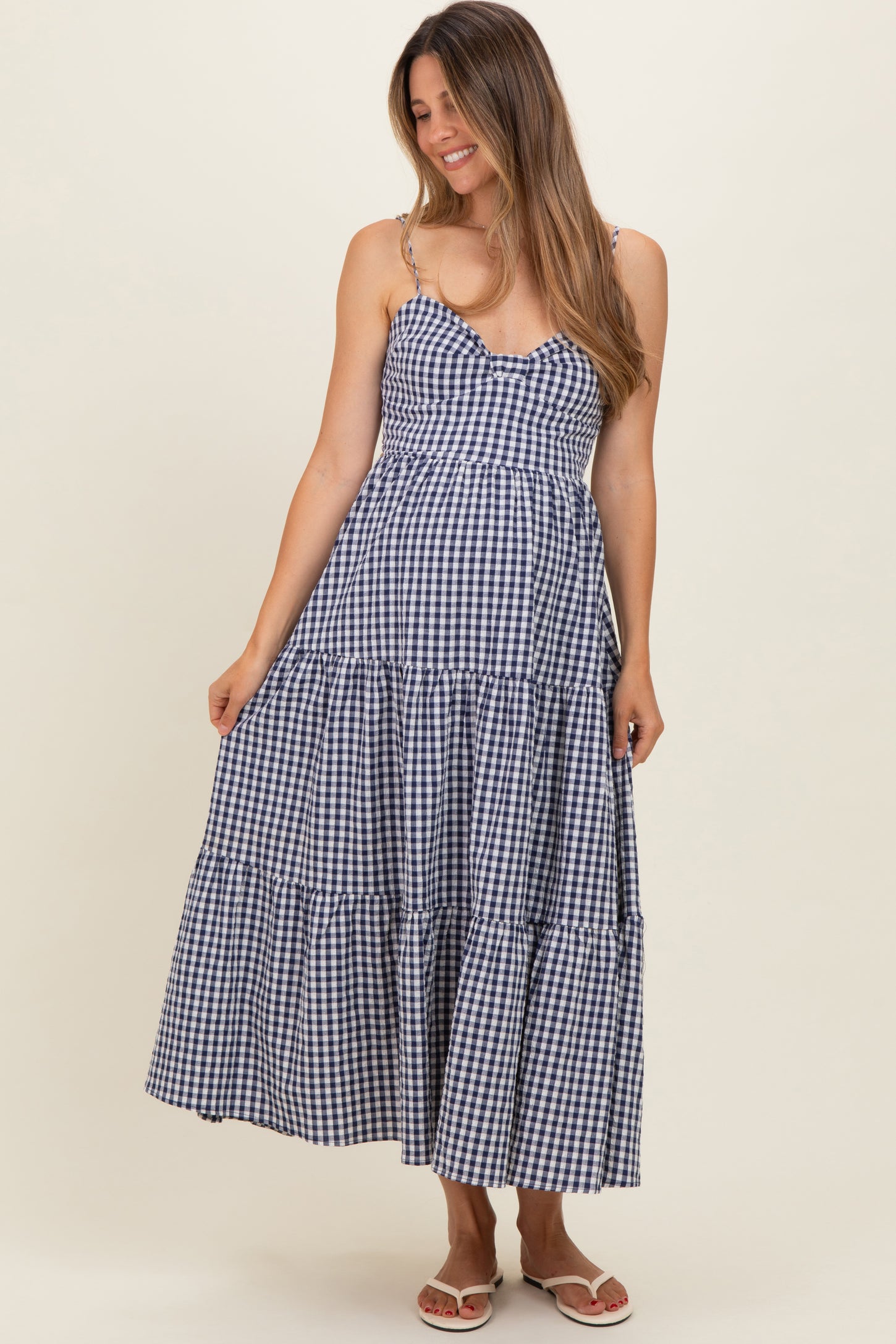 woman wearing a navy blue and white gingham print maternity dress with spaghetti straps and tiered skirt