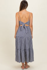 woman wearing a navy and white gingham maternity maxi dress with a cutout back and tie detail