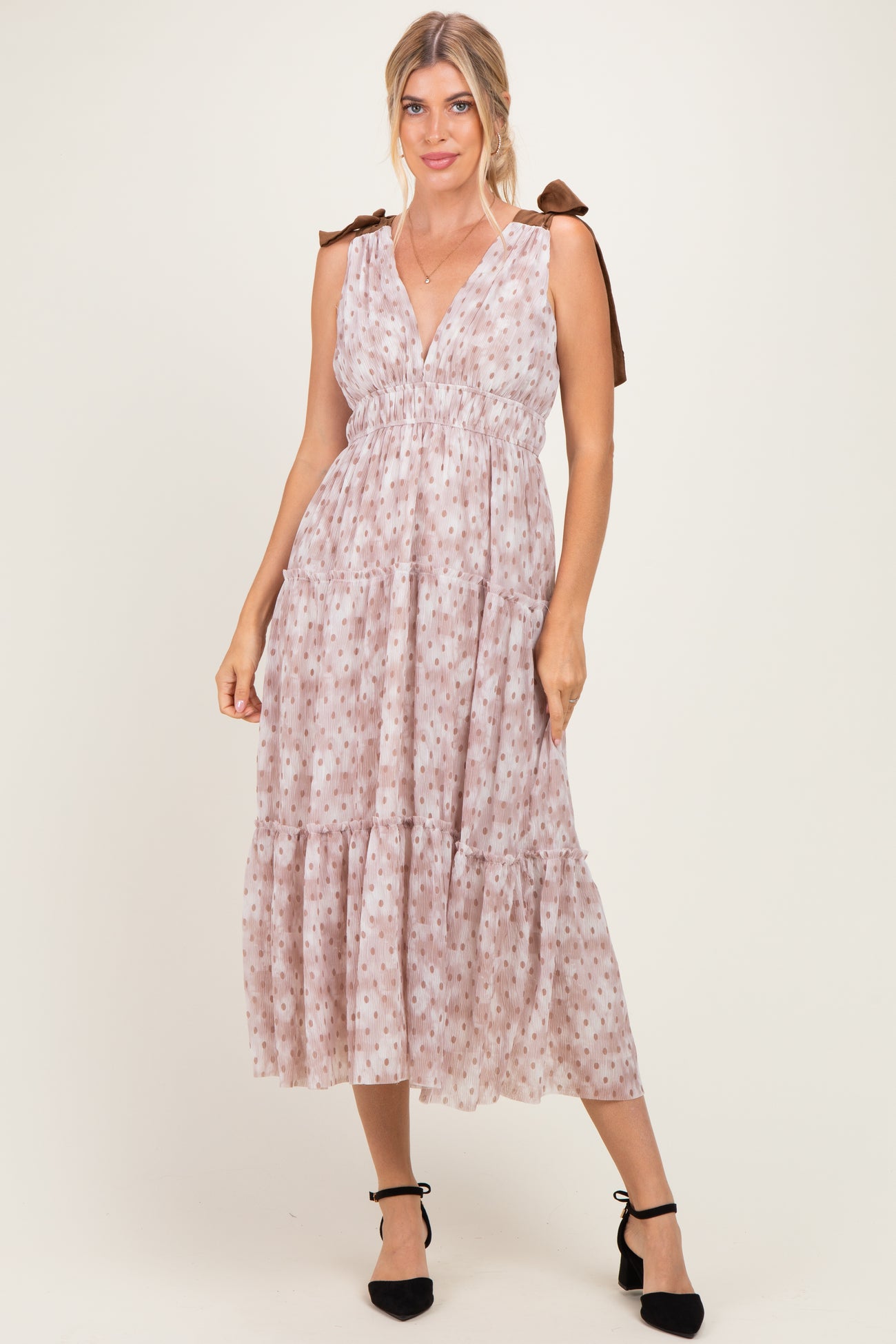 woman wearing a light pink sleeveless maxi dress with a tiered skirt and bow tie straps
