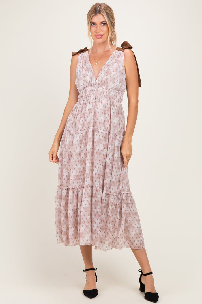 woman wearing a light pink sleeveless maxi dress with a tiered skirt and bow tie straps