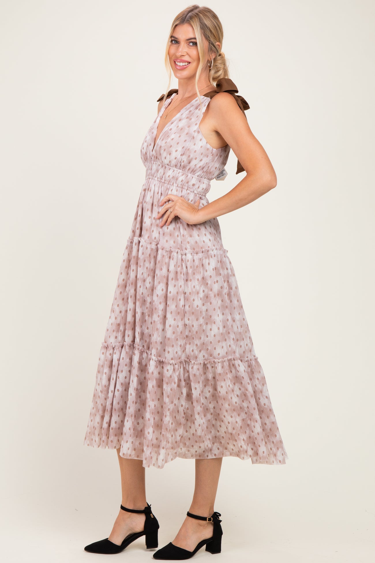 woman wearing a light pink floral midi dress with adjustable straps and a tiered skirt