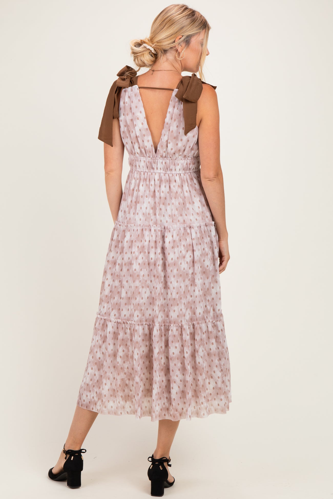 woman wearing a floral midi dress with v-back and bow tie straps in light pink and brown colors