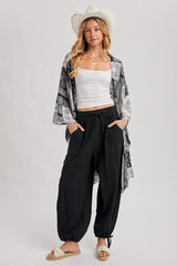 woman wearing a white tank top, black patterned kimono, and black loose-fitting pants with pockets, styled with a wide-brimmed hat