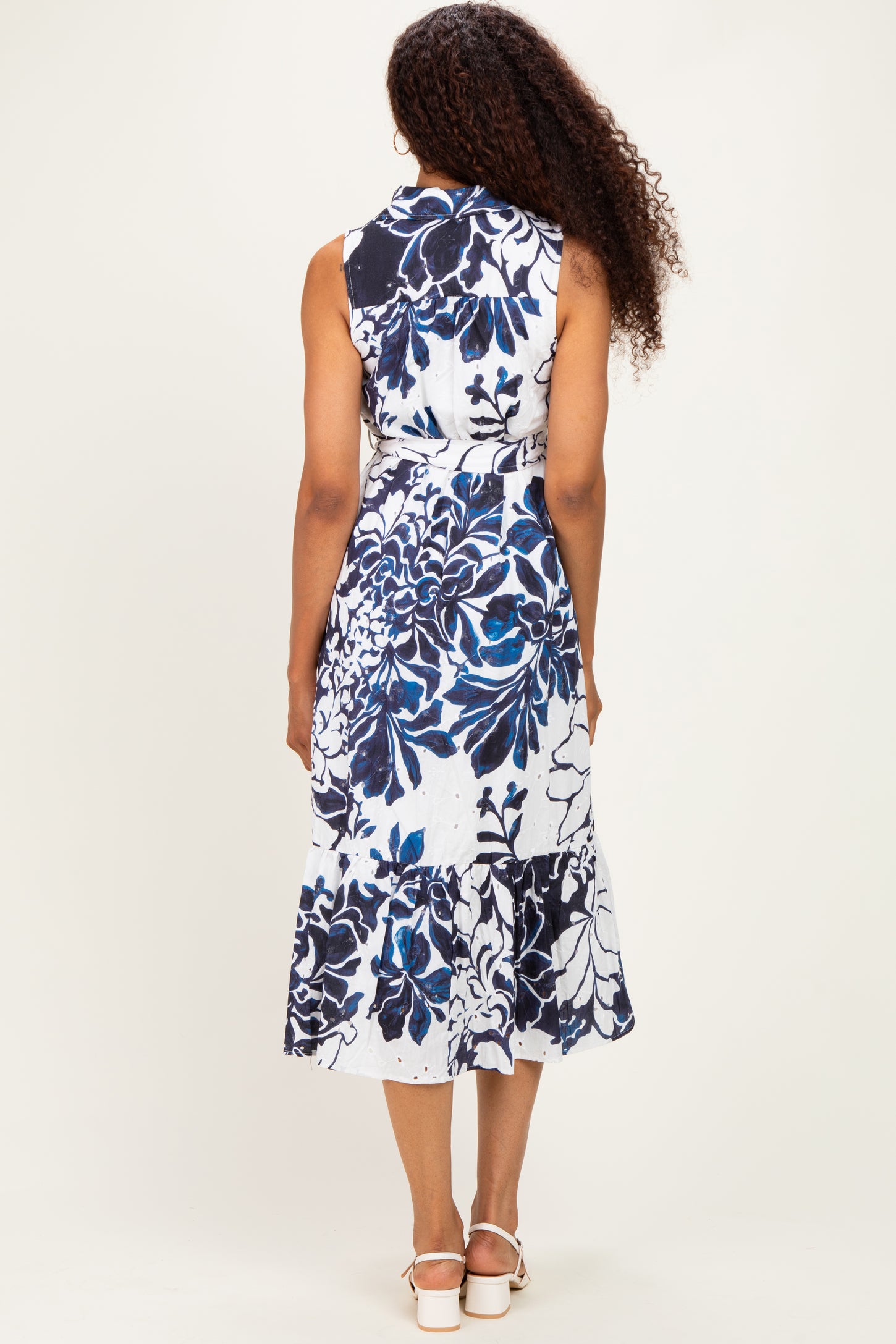woman wearing a sleeveless blue and white floral midi dress with a ruffled hem, viewed from the back