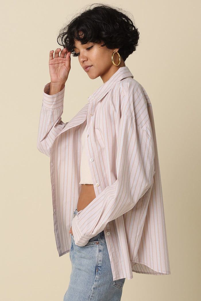 woman wearing a light pink and white striped oversized button-up shirt paired with a crop top and blue jeans