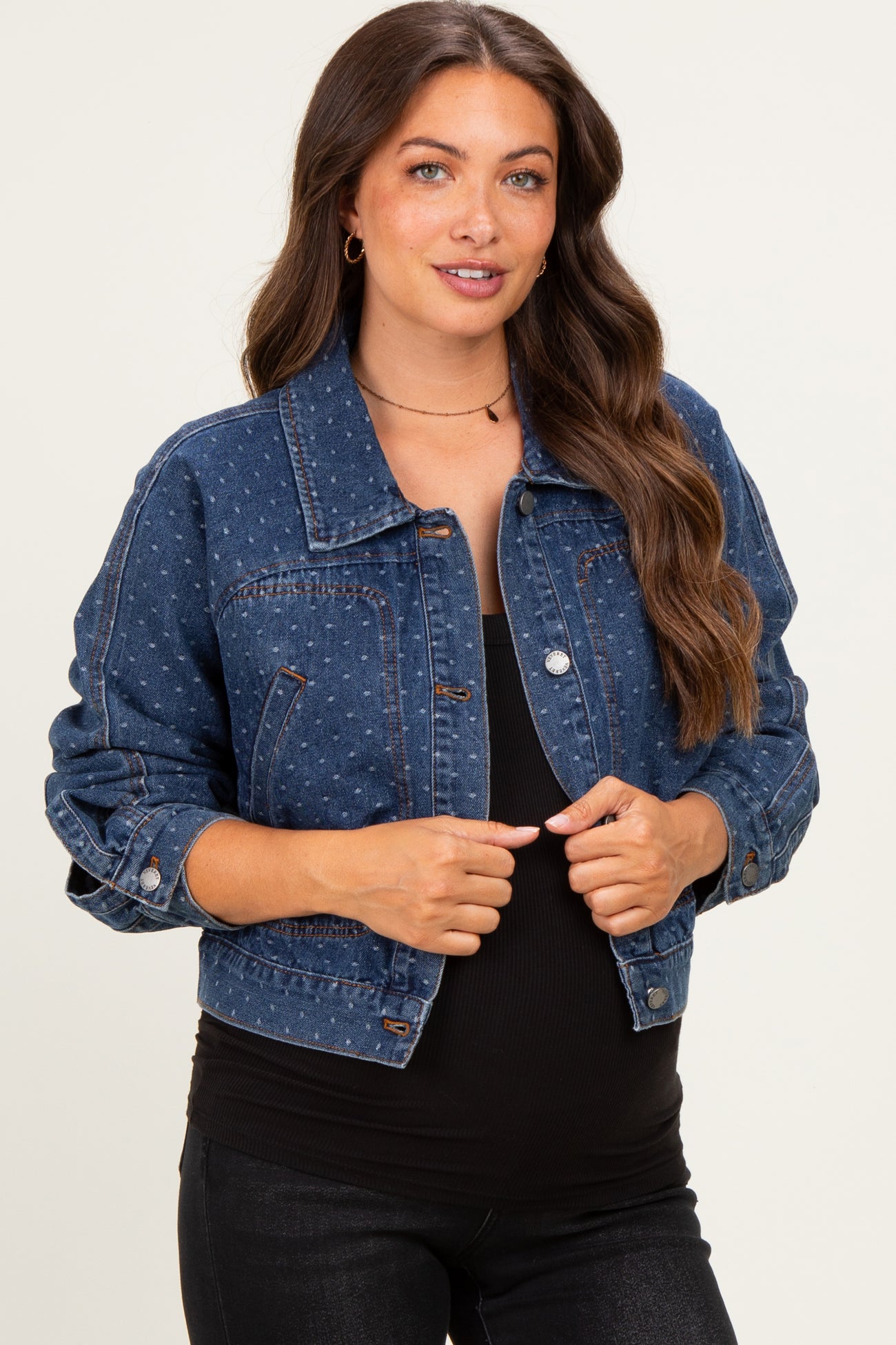 woman wearing a dark blue maternity denim jacket over a black top, smiling and showing her baby bump