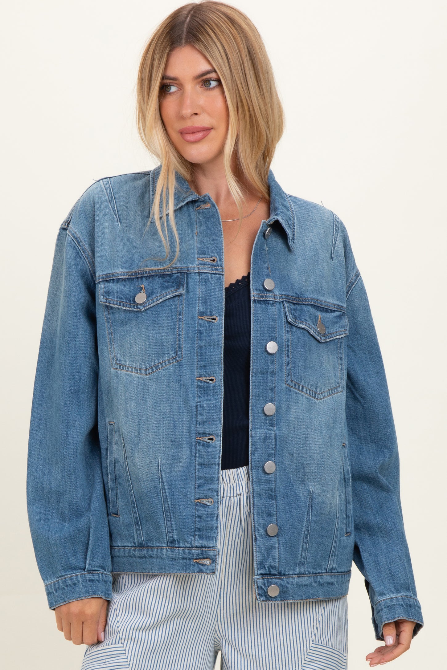 woman wearing a light wash denim jacket with front pockets and button closure, styled with a navy top and striped pants