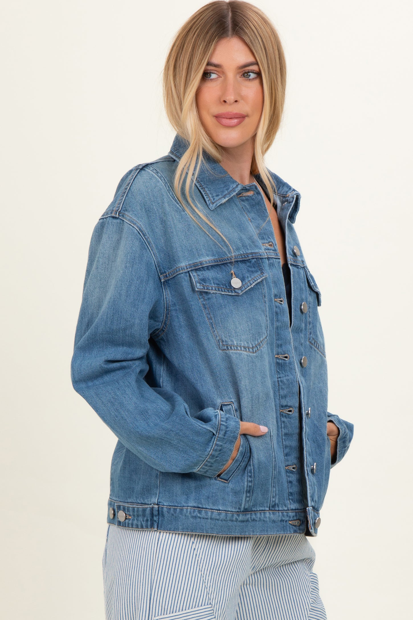 woman wearing a light wash oversized denim jacket with side pockets and a button-up front