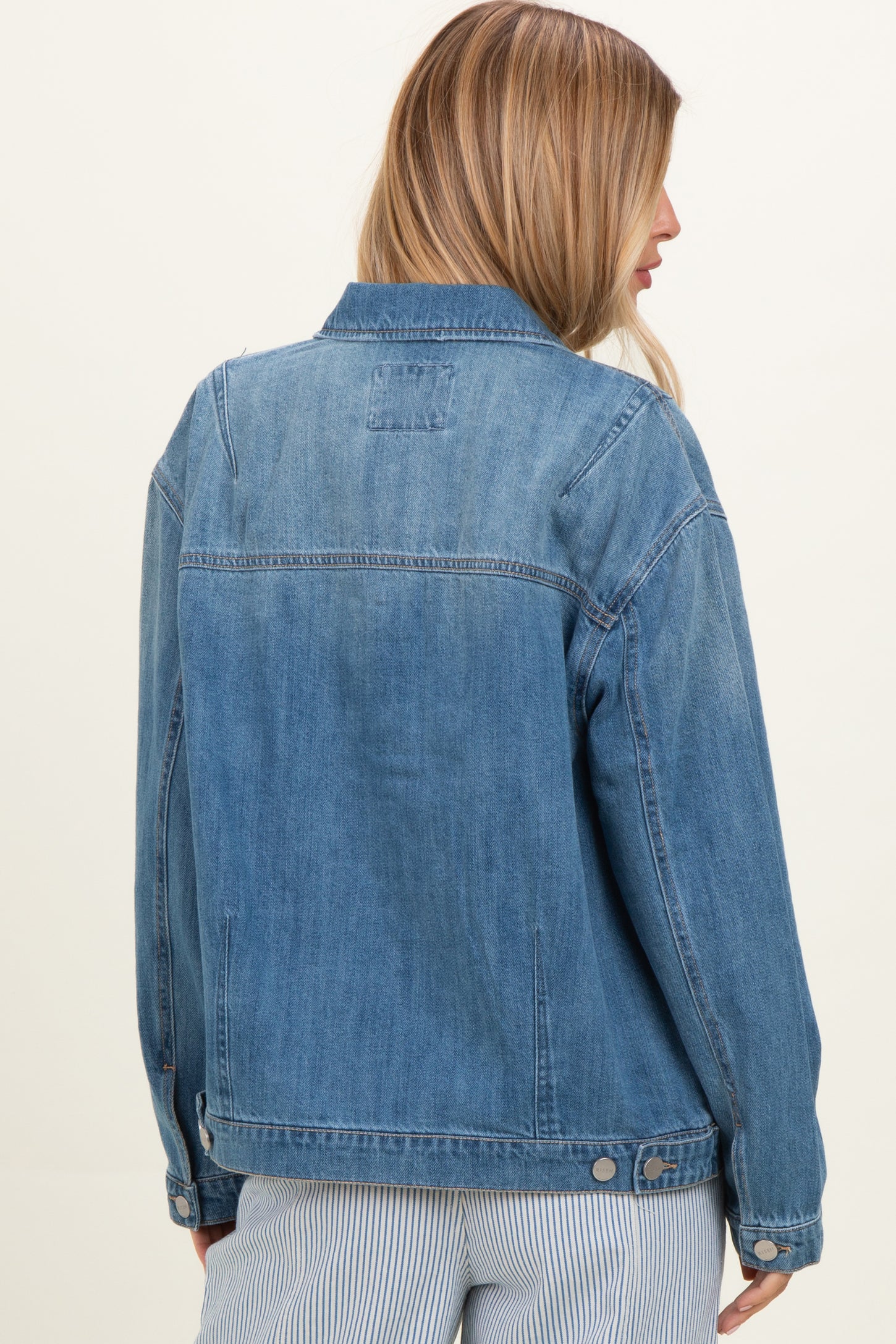 woman wearing a light blue denim jacket, viewed from the back, with a relaxed fit and classic style details