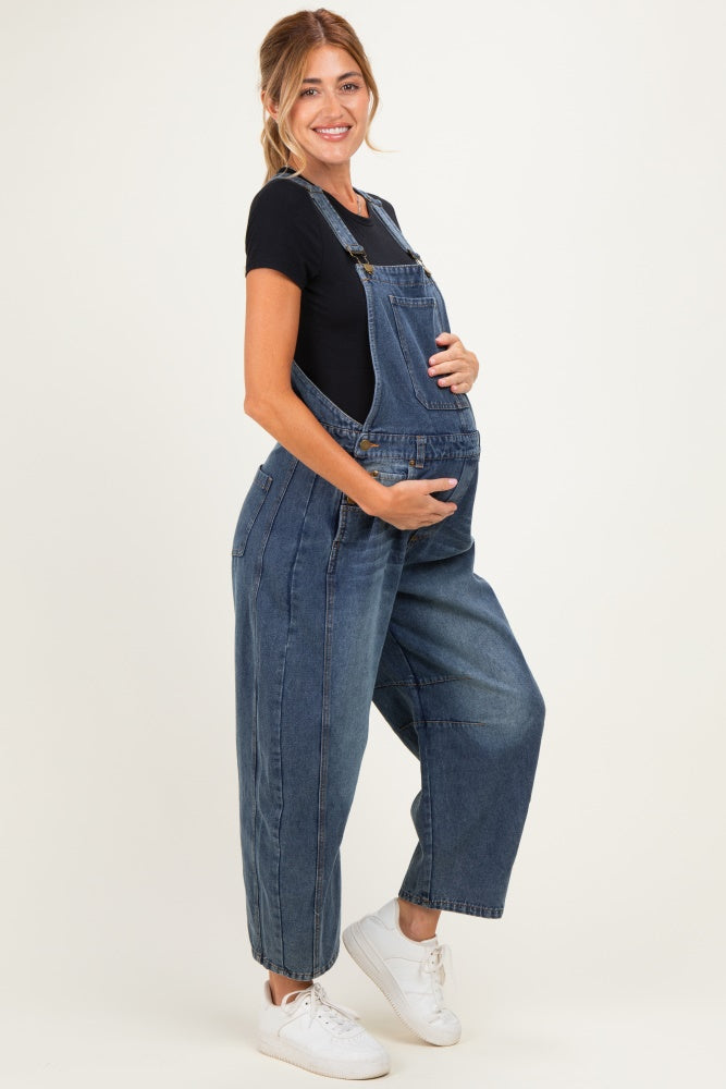 woman wearing a dark blue denim maternity overall, holding her baby bump with a black t-shirt underneath