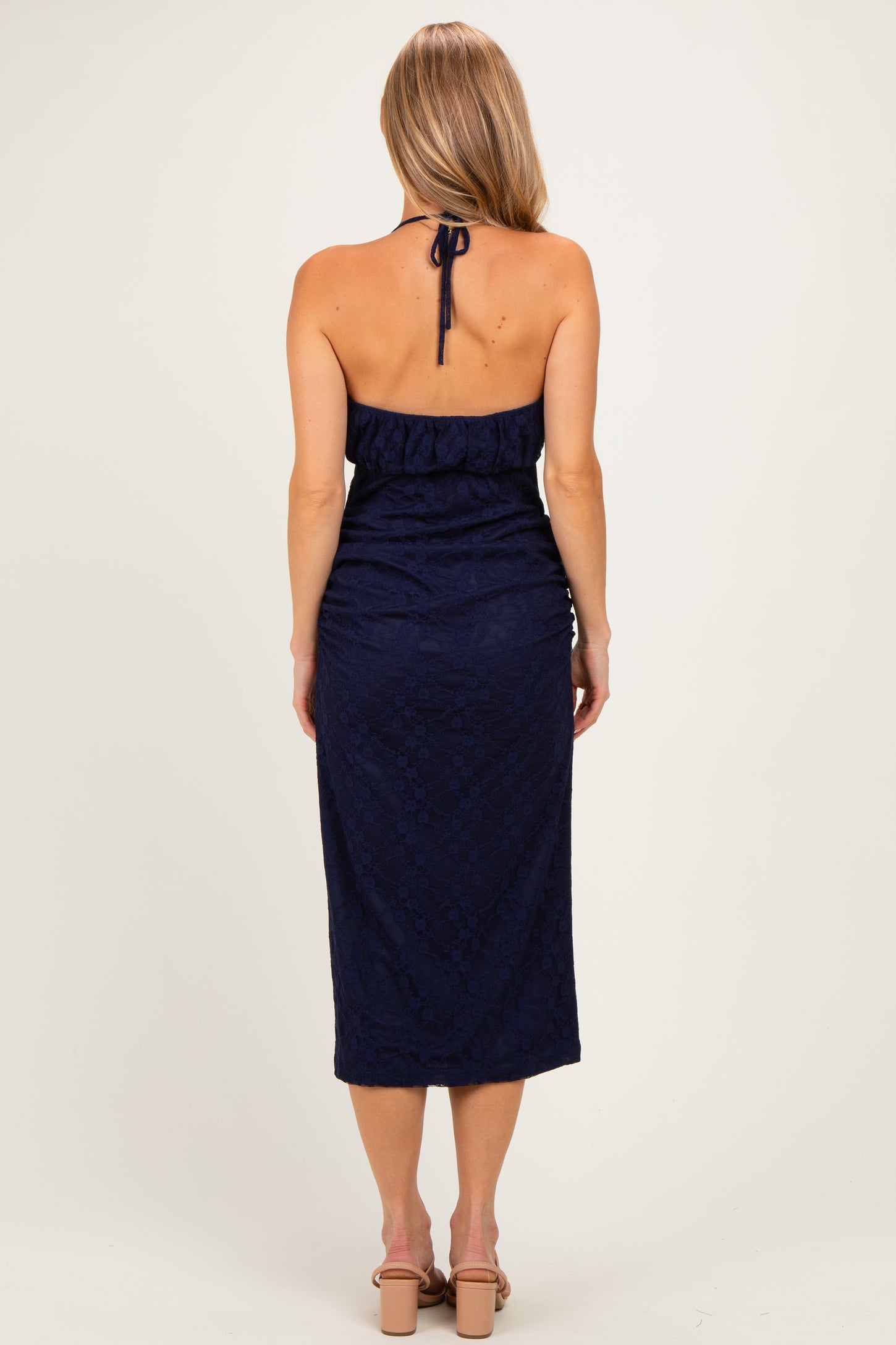 woman wearing a navy blue halter neck dress with a fitted bodice and a midi length, viewed from the back