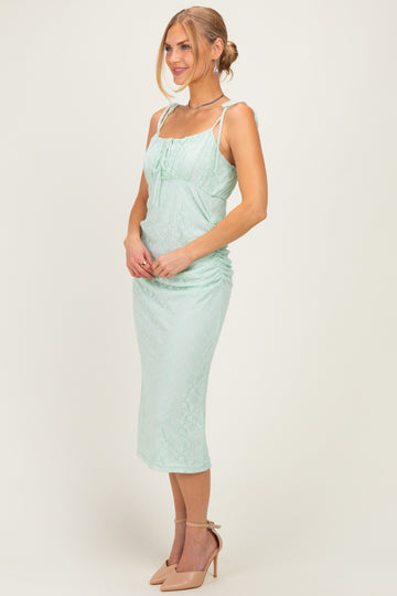 woman wearing a mint green lace midi dress with adjustable straps and ruching detail, paired with nude heels