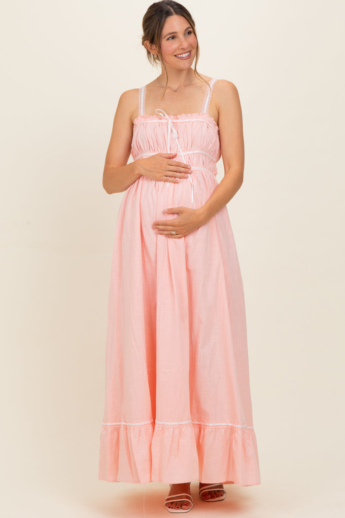 woman wearing a light pink maternity maxi dress with ruffle hem and adjustable straps, gently holding her baby bump