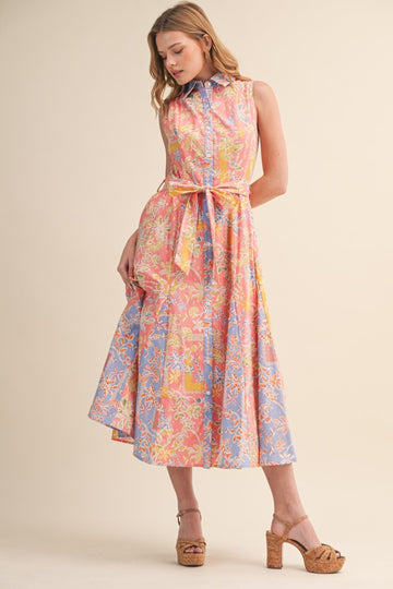 woman wearing a sleeveless pink and blue belted midi dress with a floral pattern and a collar