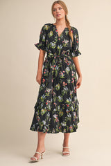 woman wearing a black floral maxi dress with ruffled sleeves and a tie waist, standing in a neutral background