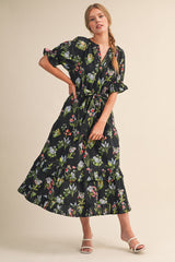 woman wearing a black floral maxi dress with short sleeves and a tiered skirt, posing with a hand on her hip