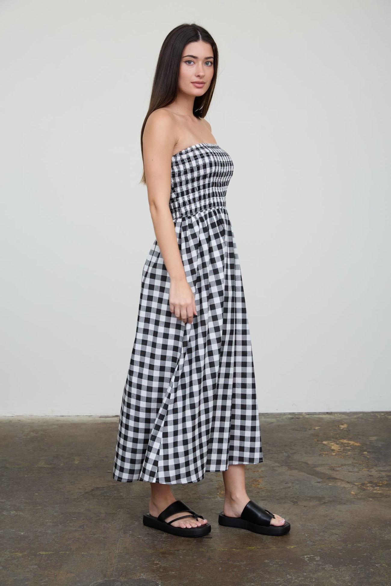 woman wearing a black and white gingham strapless maxi dress and black slide sandals