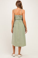 woman wearing a green and white gingham maternity dress with adjustable straps and a smocked back