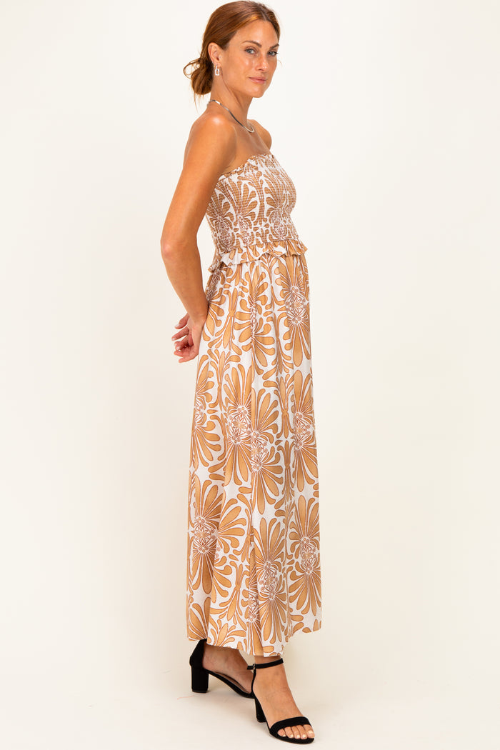 woman wearing a strapless floral maxi dress in brown and white with a ruffled waistline and a flowy silhouette