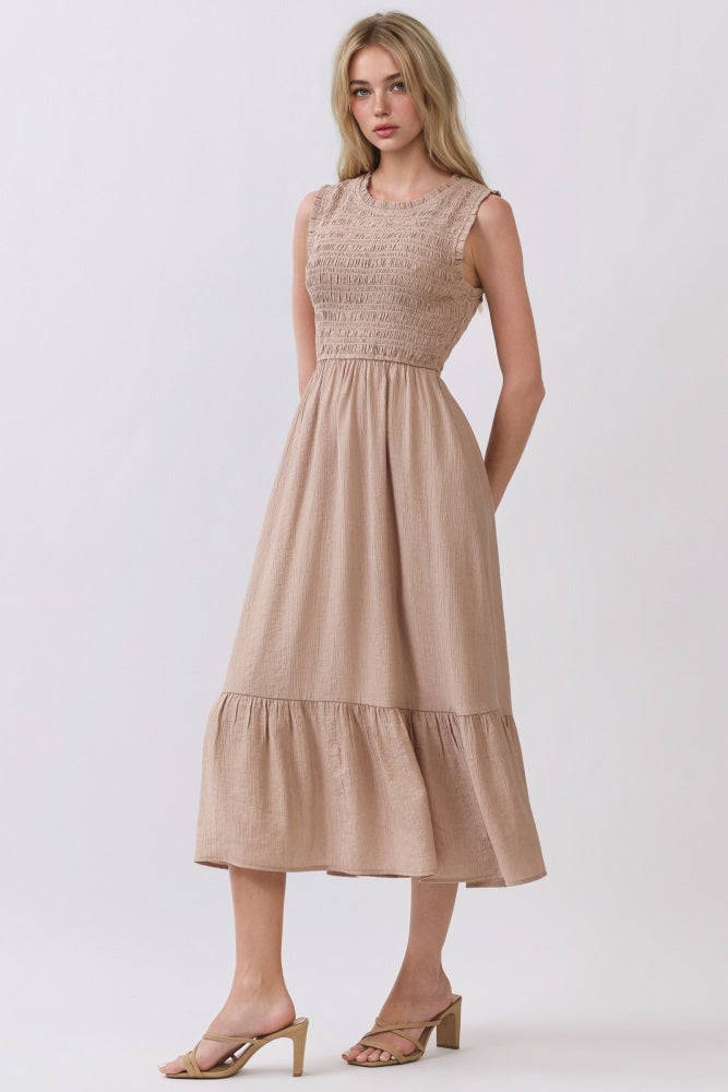 woman wearing a sleeveless light tan midi dress with a smocked bodice and tiered ruffle hem