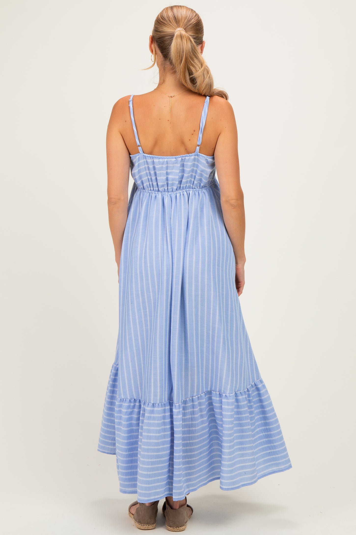 woman wearing a light blue striped maxi dress with spaghetti straps and a tiered ruffle hemline, viewed from the back
