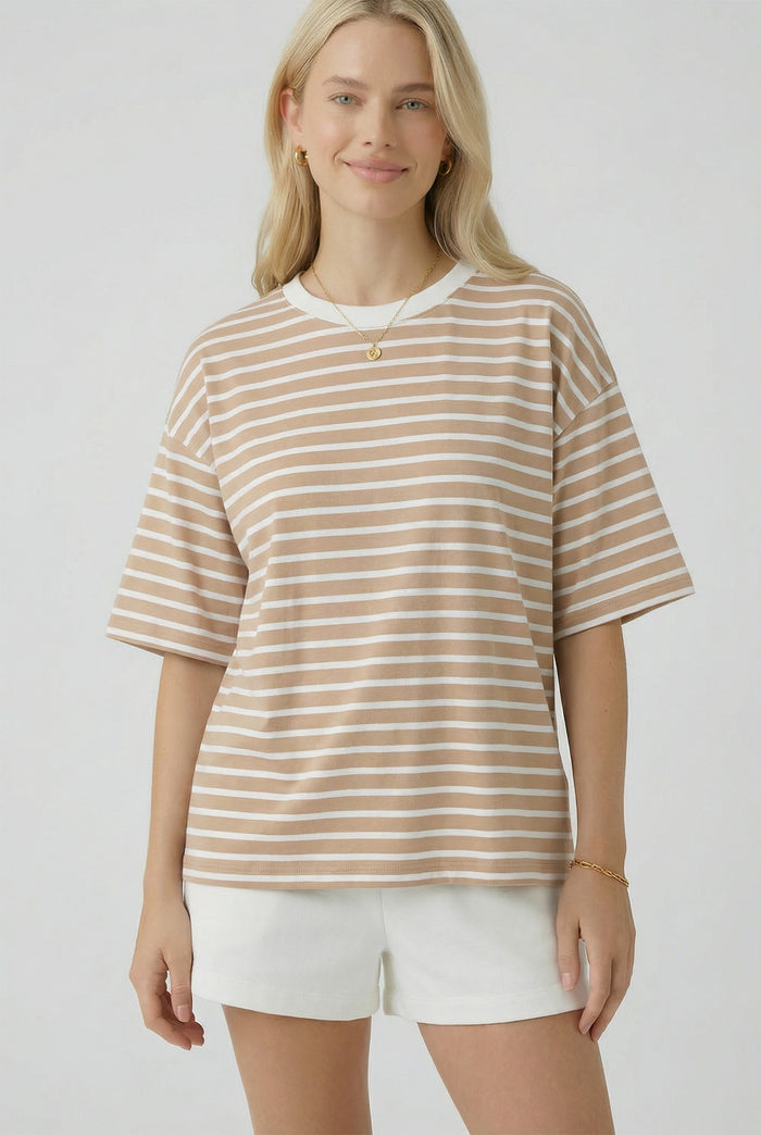 woman wearing a beige and white striped oversized t-shirt with short sleeves and standing with a slight smile