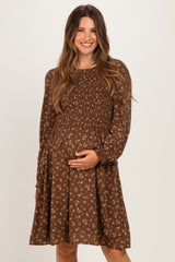 woman wearing a brown floral maternity dress with smocked bodice and long sleeves, holding her baby bump