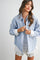 woman wearing a light blue striped oversized button-up shirt with white cuffs and a white lace mini skirt