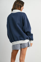 woman wearing a navy blue oversized sweatshirt with a white collar and gray trim, paired with checkered shorts