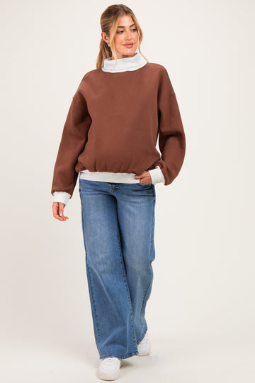 woman wearing a brown oversized maternity sweatshirt with a white collar and cuffs, paired with wide-leg jeans