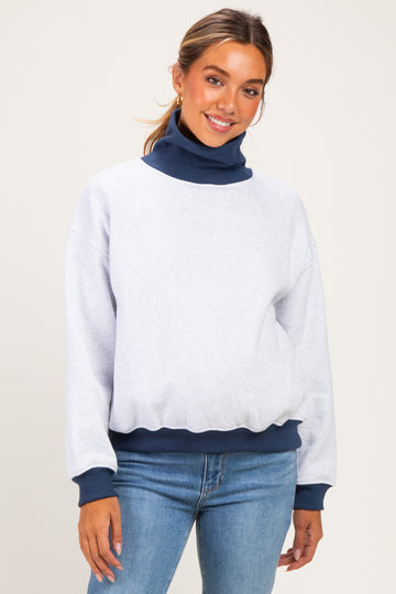 woman wearing a gray maternity sweatshirt with a navy turtleneck and cuffs, styled with jeans